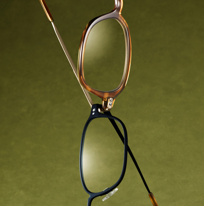 Two pairs of glasses, one tortoise-shell and one black, are hanging and overlapping on a green background.