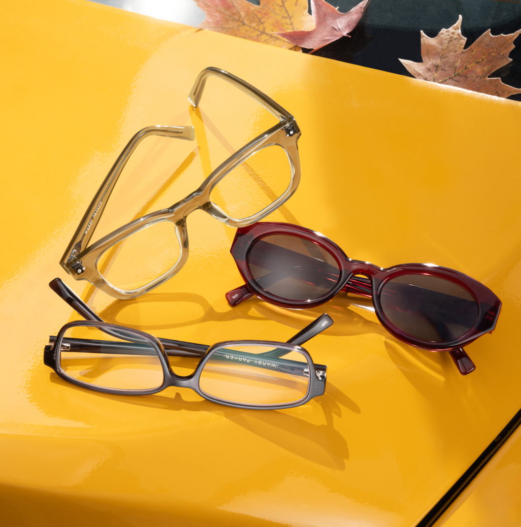 Three pairs of glasses on a yellow surface with autumn leaves.