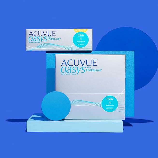 Boxes of contact lenses (Air Optix, Biofinity, Acuvue Oasys) and a Warby Parker lens case on a blue tiled surface.