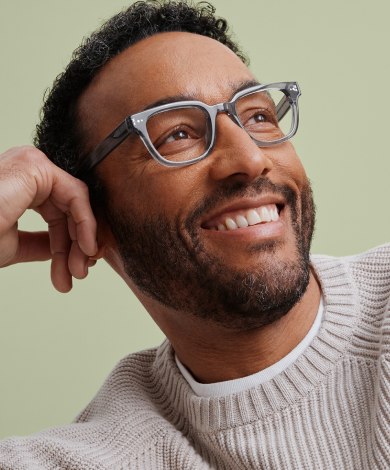 A man with a beard and glasses smiles as he leans his head on his hand.