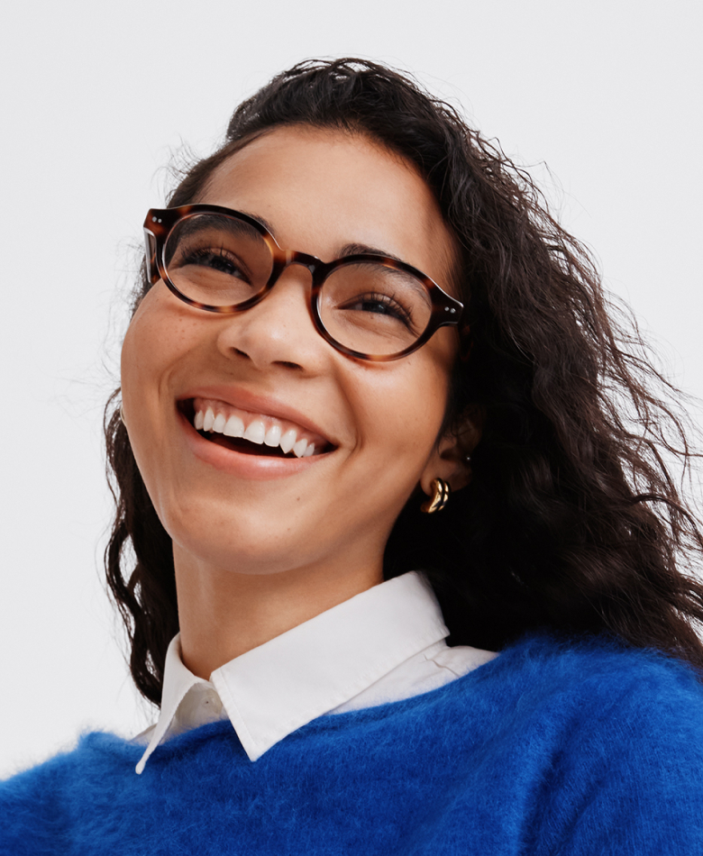 Close-up of a dark-skinned woman wearing tortoiseshell cat-eye sunglasses and a green sweater.