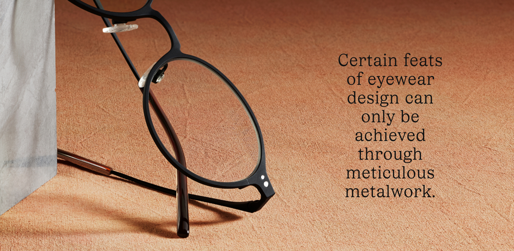 A close-up of a pair of eyeglasses with a thin black frame, resting on a textured surface.