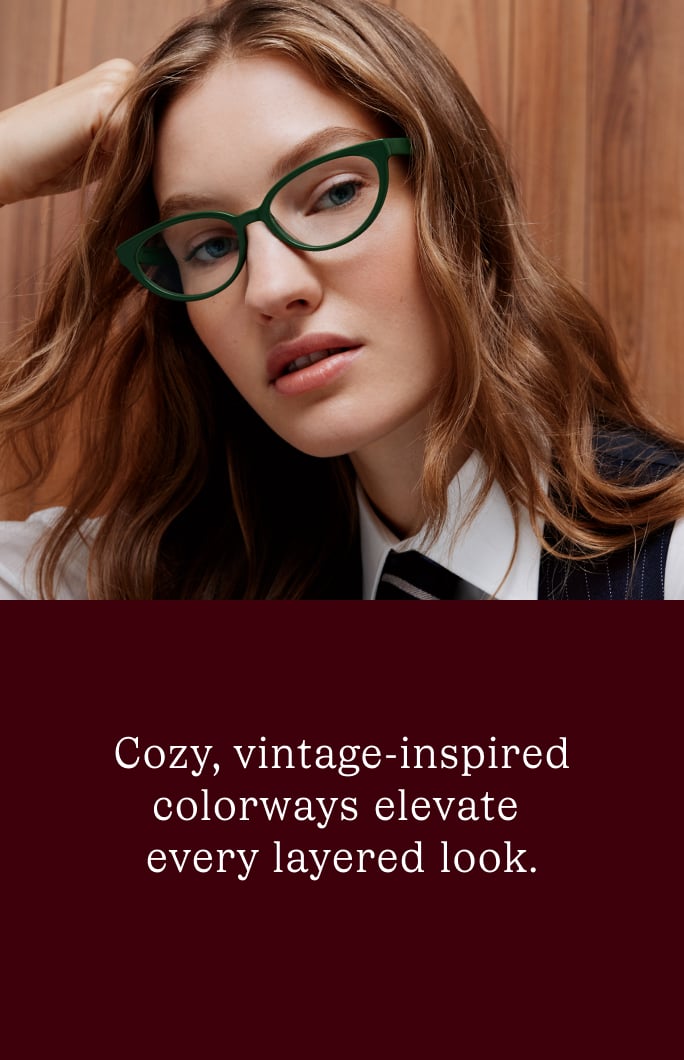 A woman wears green cat-eye glasses, complementing her layered outfit.