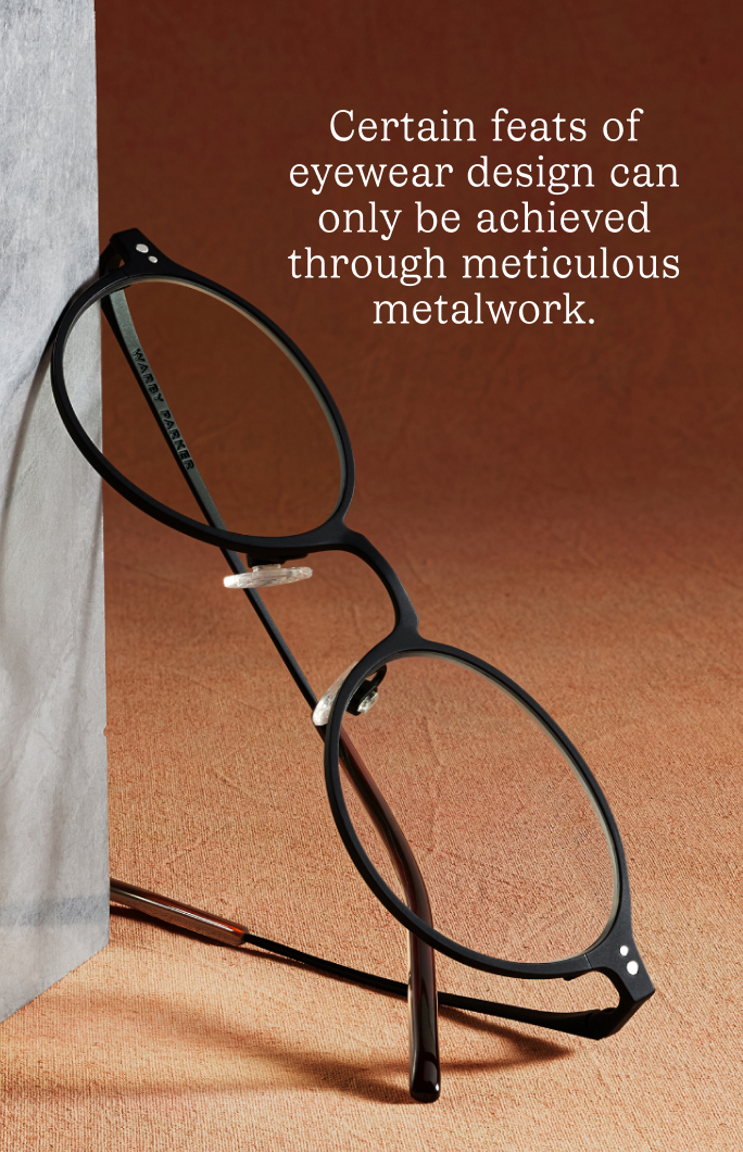 Black metal-framed eyeglasses resting against a textured surface, with text about eyewear design.