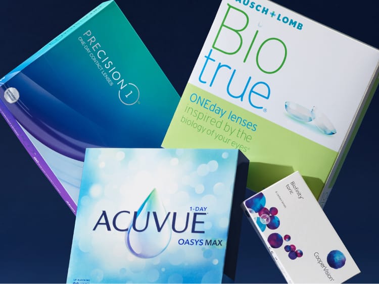 Boxes of Precision1, Biotrue, Acuvue Oasys Max, and Biofinity contact lenses on dark surface.