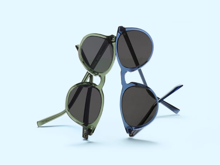 Pair of green sunglasses and pair of blue sunglasses with dark lenses on a light blue surface.